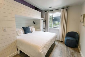 Une chambre à coucher avec un lit, une chaise, une fenêtre avec des rideaux et une vue sur l’extérieur.