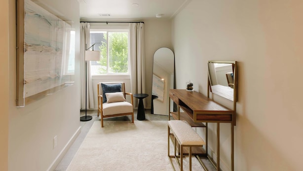 A room with a large window, a chair, a small table, a mirror, and a wall-mounted artwork. - Rooftop Patio Downtown GH: Steps to Lake & Dining (Grand Haven)