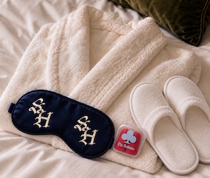 A neatly arranged set of white towels, a pair of slippers, and a sleep mask on a bed. - The Solitaire Hotel (Vancouver)