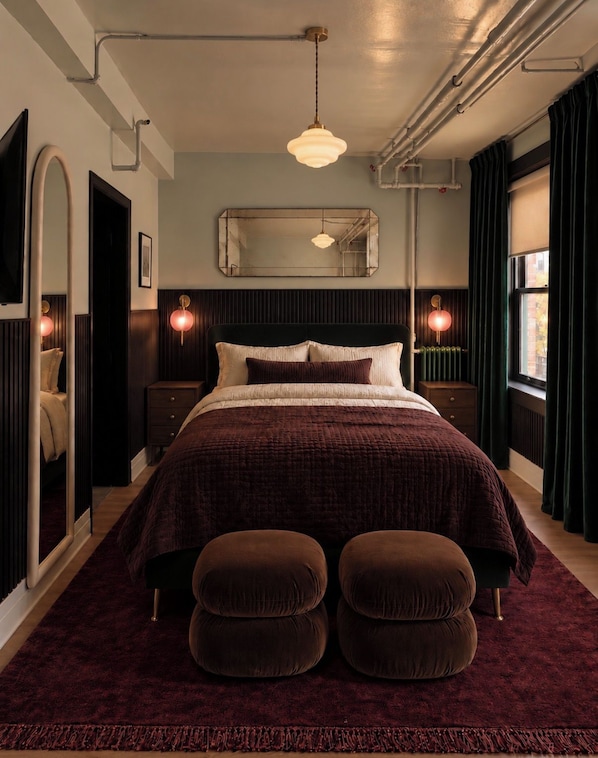 A modern bedroom with a large bed, two bedside tables, a mirror, and a window with curtains.