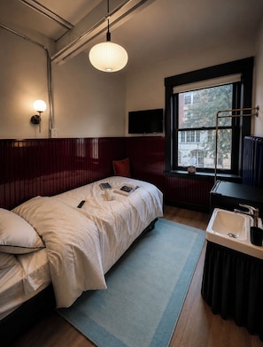 A bedroom with a bed, a bedside table, a window, a television, and a radiator. - The Solitaire Hotel (Vancouver)