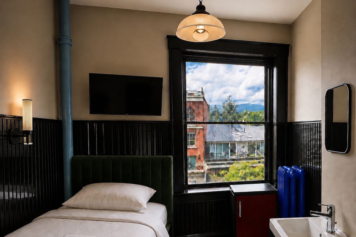A hotel room with a bed, a window with a view, a bedside table, and a bathroom.