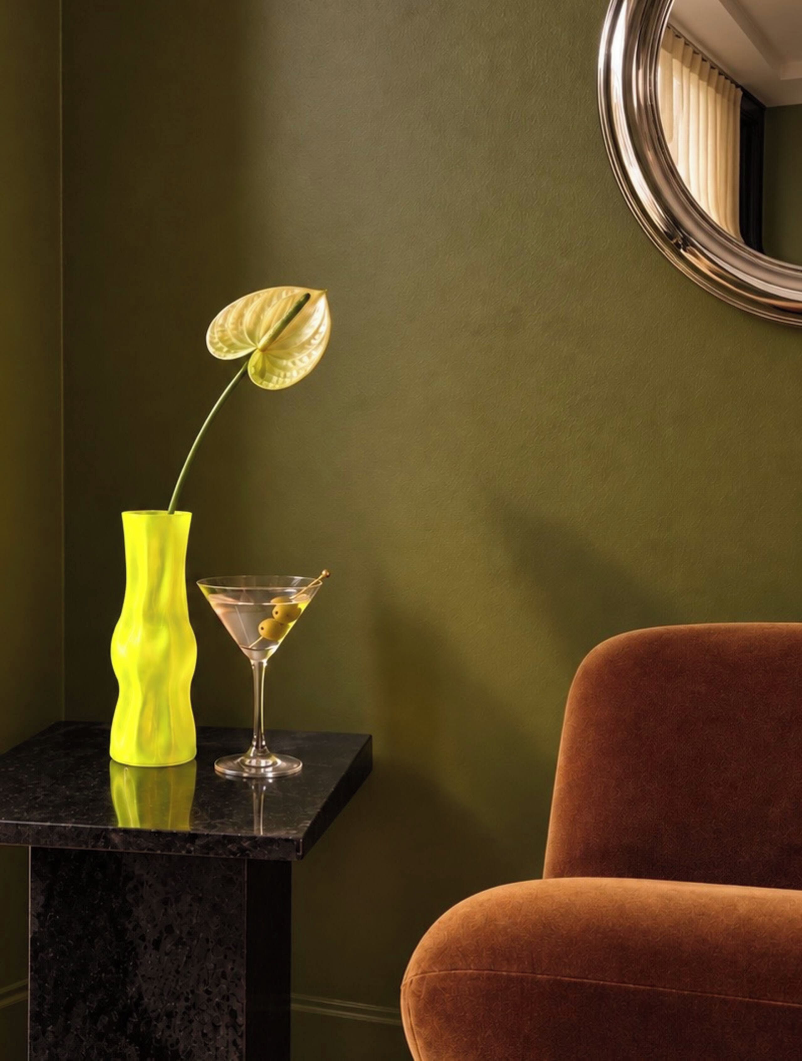 Ein Zimmer mit einem schwarzen Marmor-Beistelltisch, einer gelben Vase mit einer Pflanze und einem Martini-Glas mit Zitronenzeste.
