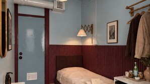 A compact bedroom with a bed, bedside table, and a small kitchenette. - The Solitaire Hotel (Vancouver)
