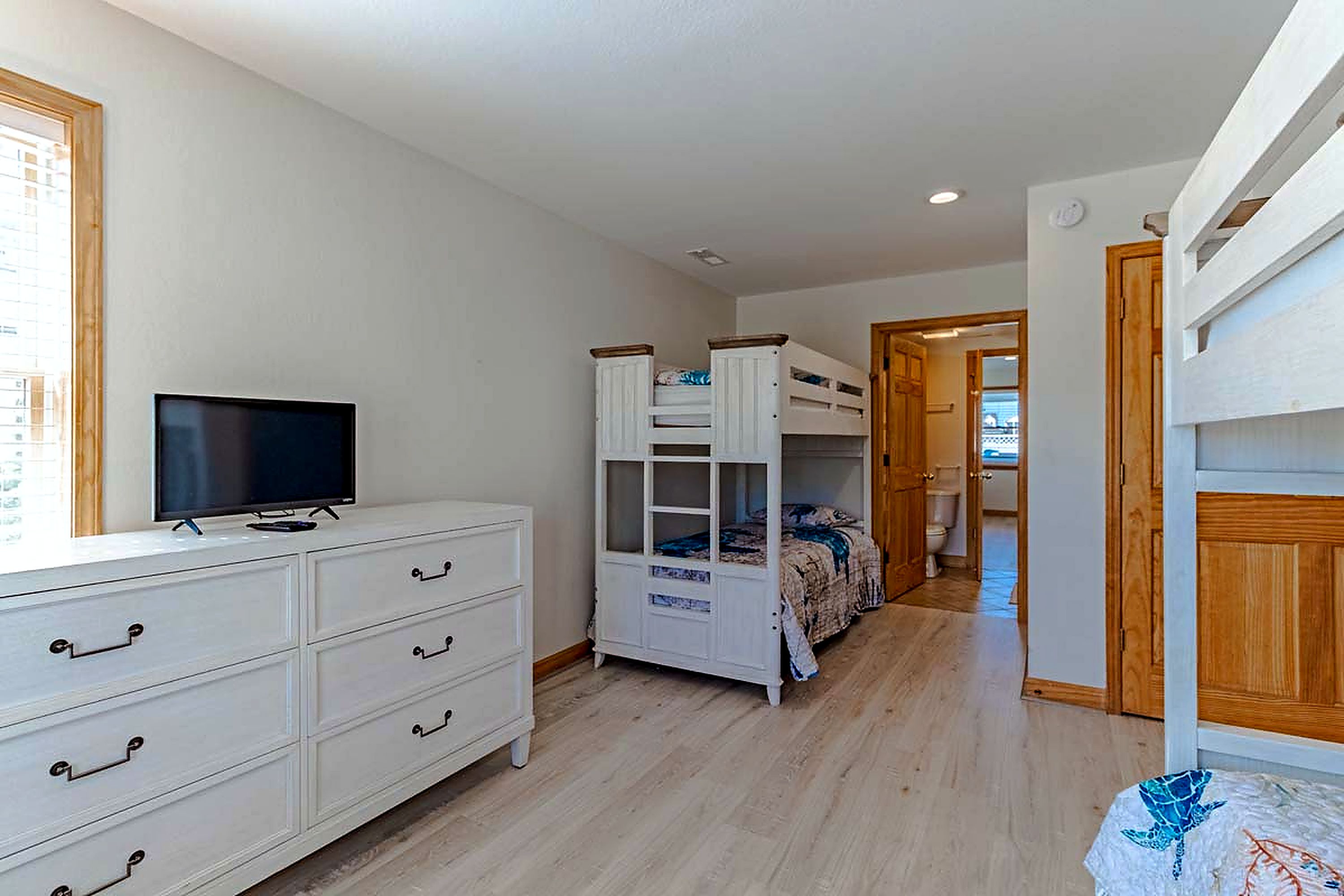 Une chambre avec une télévision, une commode blanche, un lit superposé et une porte en bois.