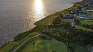 An aerial view of a golf course with a large body of water on one side and a residential area on the other. - 🏖️ Luxury 8BR🌊 Ocean Views💦 Free Pool Heat♨️ Elevator🐾2nd Row✨Pet Friendly (Nagshead)