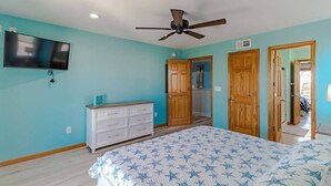 A bedroom with a bed, a ceiling fan, a television, and wooden doors. - 🏖️ Luxury 8BR🌊 Ocean Views💦 Free Pool Heat♨️ Elevator🐾2nd Row✨Pet Friendly (Nagshead)