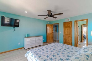 Ein Schlafzimmer mit Bett, Deckenventilator, Fernseher und Holztüren.