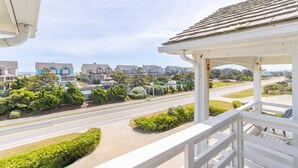 A residential street with houses, a clear sky, and a white balcony railing. - 🏖️ Luxury 8BR🌊 Ocean Views💦 Free Pool Heat♨️ Elevator🐾2nd Row✨Pet Friendly (Nagshead)