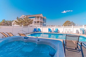 Une piscine dotée de chaises longues et d’un jacuzzi, entourée d’une clôture et avec un bâtiment visible à l’arrière-plan.