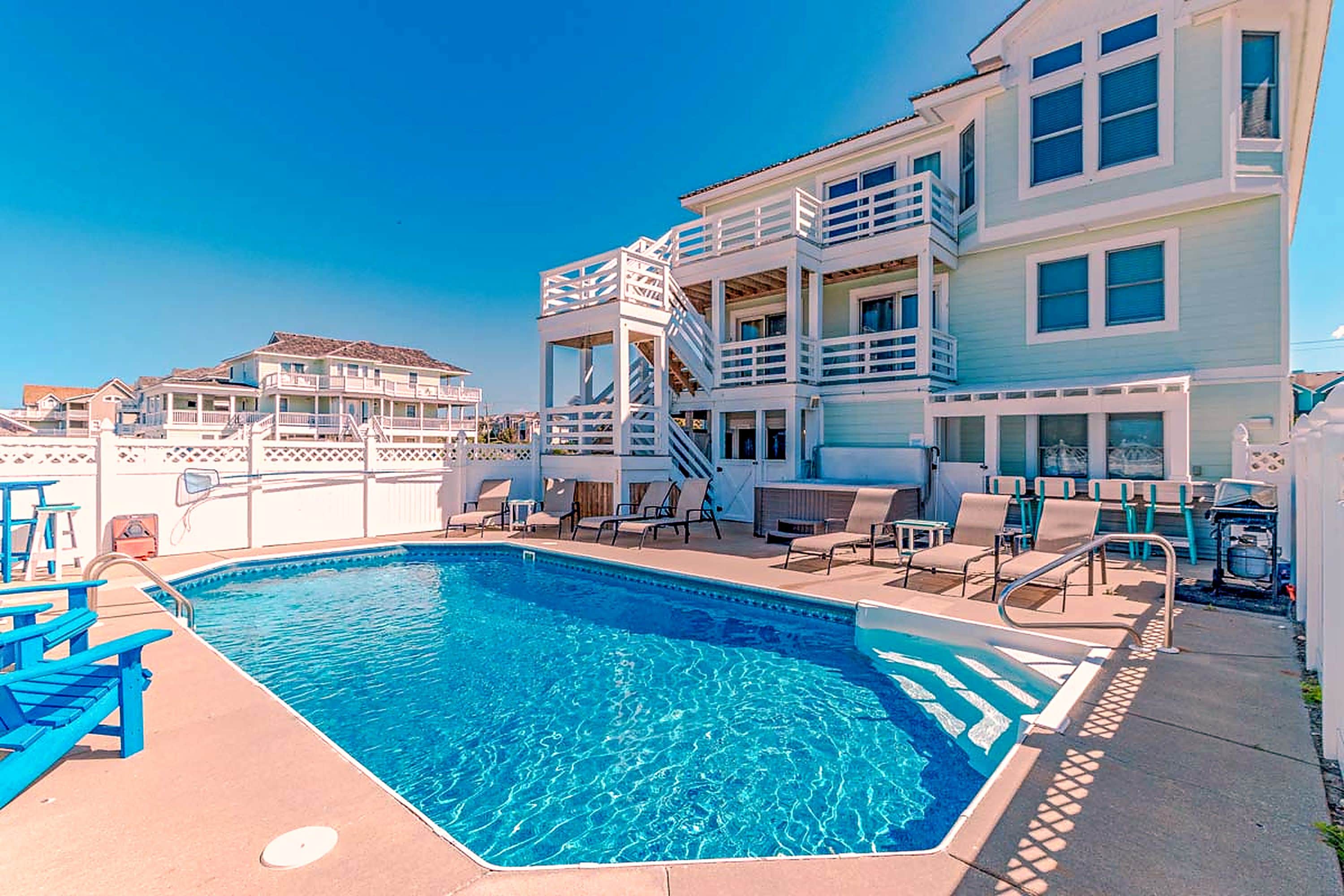 A swimming pool with a clear blue water, surrounded by lounge chairs and a building with multiple balconies.