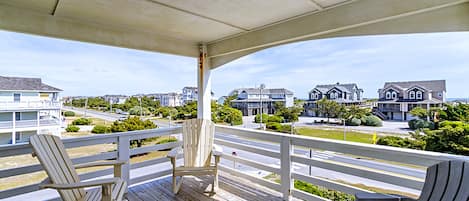 A wooden deck with two Adirondack chairs, overlooking a residential street with houses.