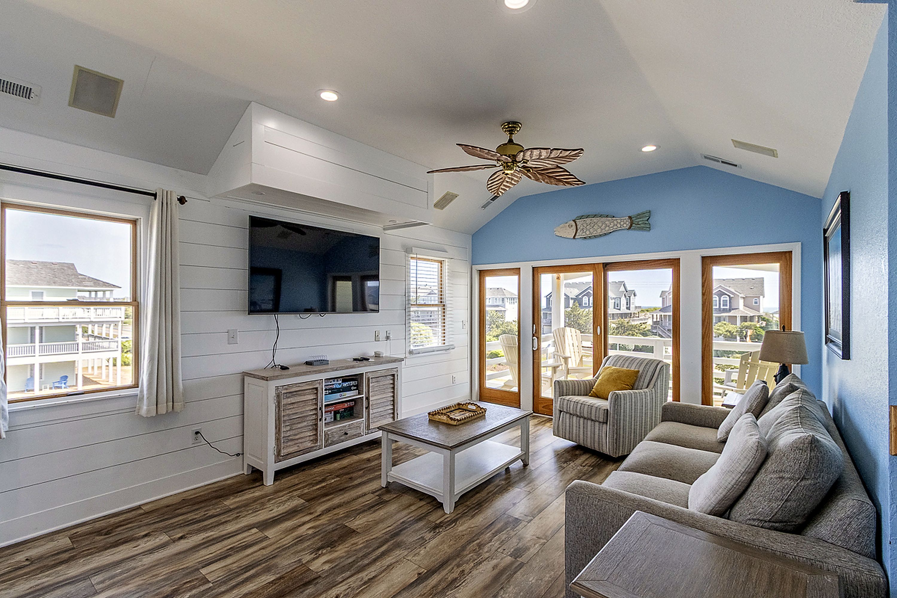 A living room with a wooden floor, a white entertainment unit, a ceiling fan, and a view through a glass door.