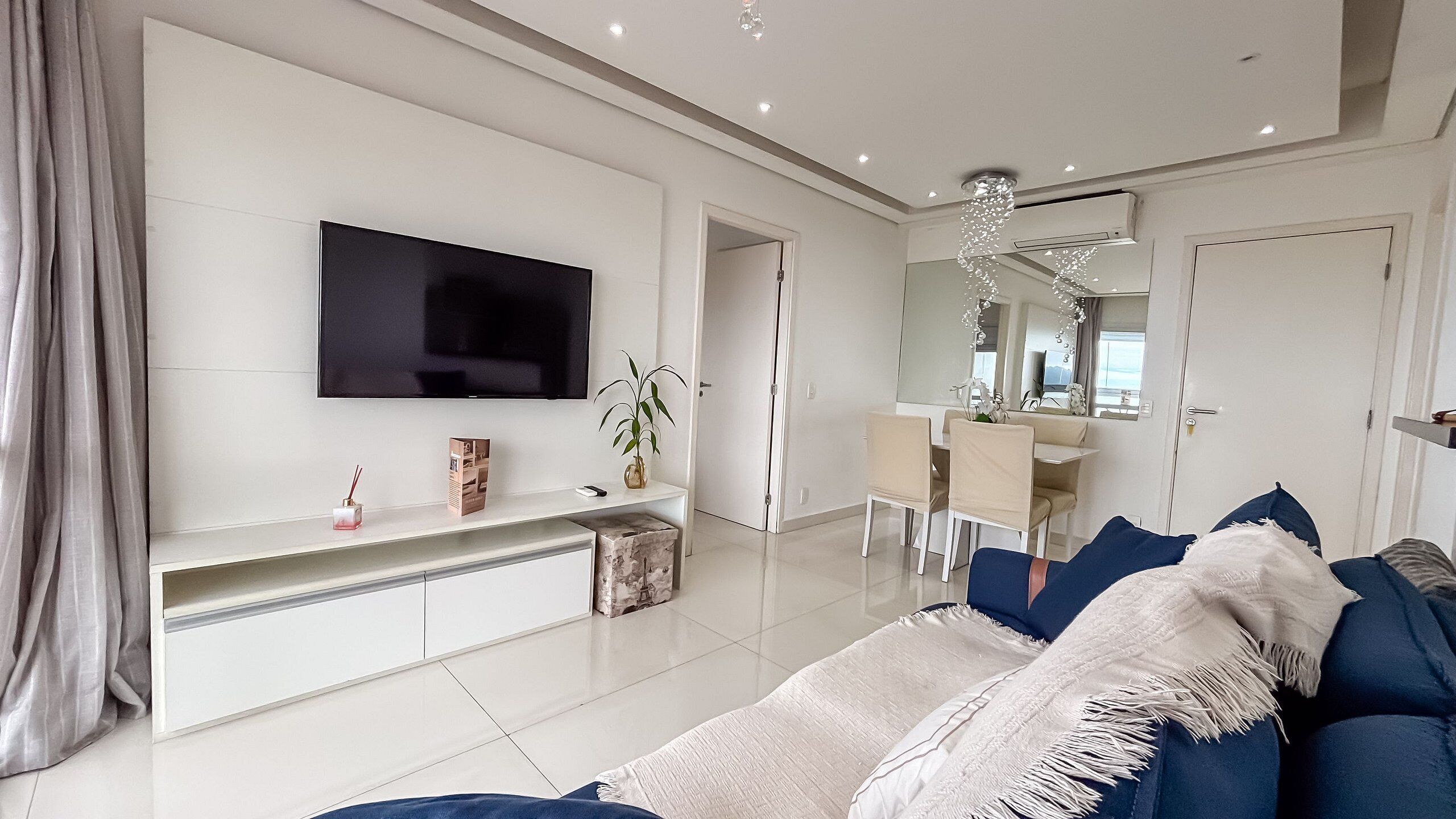 A modern living room with a flat-screen TV, a dining area, and a large mirror.