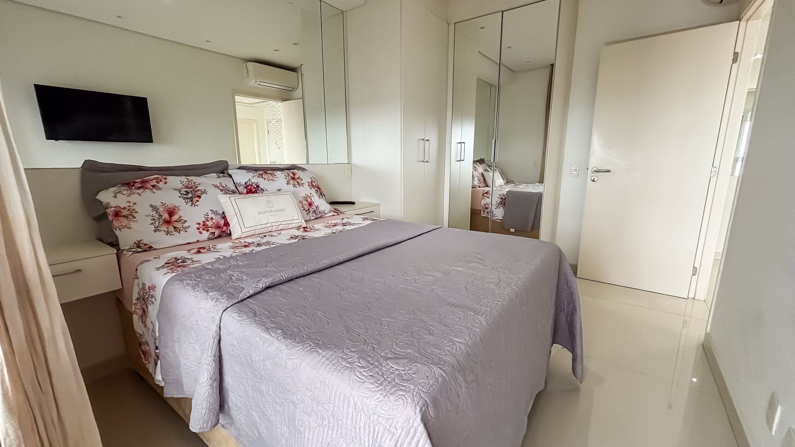 Un dormitorio con cama, mesita de noche, televisor, armario y espejo.