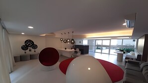 Et moderne interiør med et stort, hvidt og rødt, kugleformet siddeområde, en hvid sofa og en vægmonteret lampe.