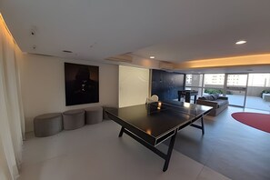 Una habitación moderna con mesa de ping pong, sofá y un amplio ventanal que ofrece vistas a la ciudad.