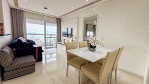 Una sala de estar moderna con sofá, mesa de comedor con sillas, televisor y balcón con vistas.
