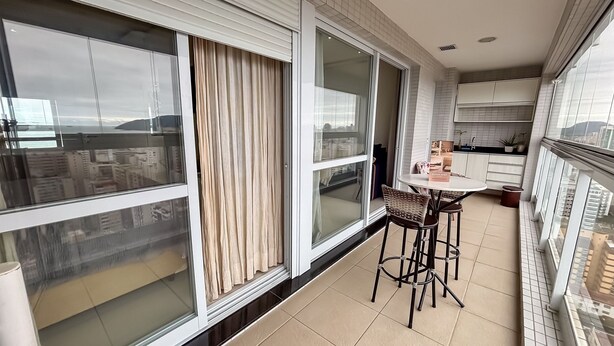 En moderne lejlighed med store vinduer, balkon, køkken med hvide skabe og spiseområde med bord og stole.