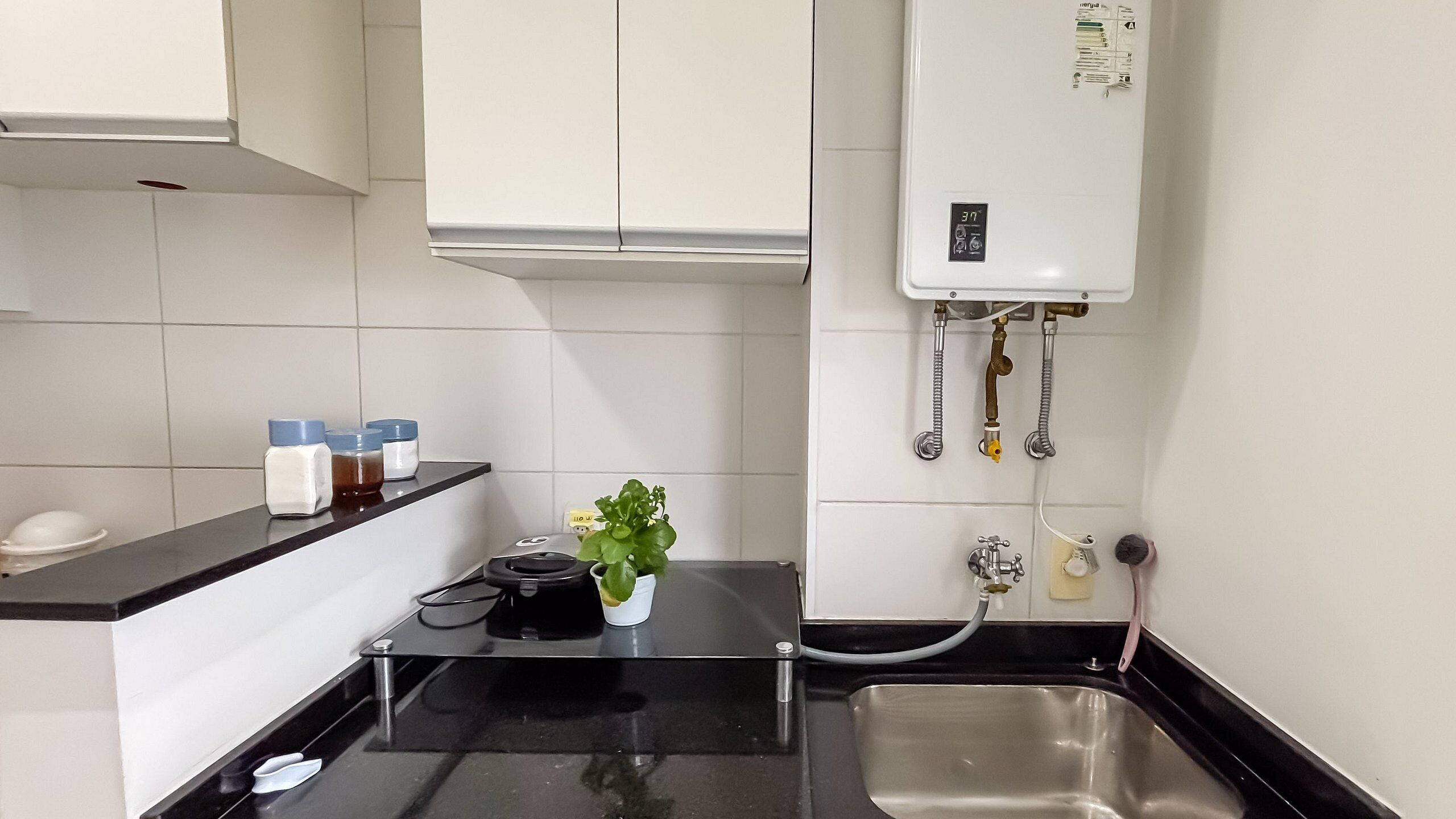 Una cocina compacta con encimera negra, pileta de acero inoxidable y calentador de agua instalado en la pared.