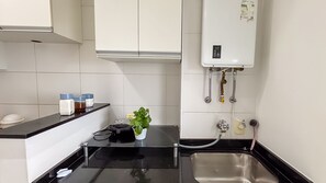 Una cucina compatta con un piano di lavoro nero, un lavello in acciaio inossidabile e uno scaldabagno a parete.