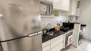 Uma cozinha com geladeira de aço inoxidável, pia, fogão e armários brancos.