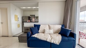Un soggiorno con un divano, un poggiapiedi decorato e una cucina sullo sfondo.