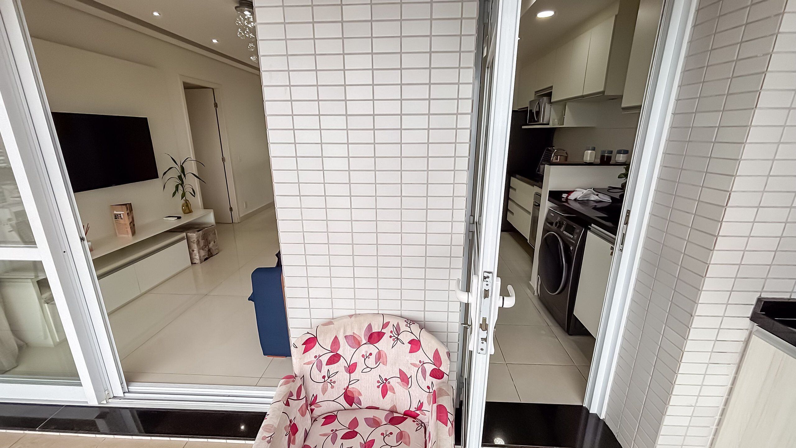 Een moderne keuken met witte tegels, een wasmachine en een televisie aan de muur.