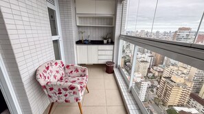 Un balcón con una silla, un cesto de basura pequeño y una zona de cocina con armarios y un lavabo.