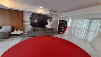 Un salón moderno con un tapete circular rojo grande, un sofá gris, una mesita redonda pequeña y una estantería.