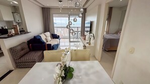 En moderne stue med sofa, spisebord og byudsigt gennem store vinduer.