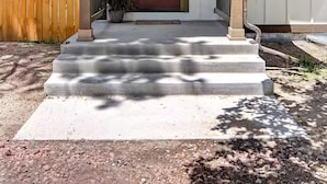 A residential property with a front porch, a wooden fence, and a driveway leading to a garage. - The little Beach House in the Forest (Colorado Springs)