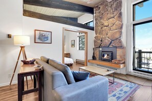 Ein modernes Wohnzimmer mit Kamin aus Stein, einer Couch, einer Lampe und Blick durch ein großes Fenster.