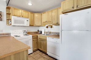 A compact kitchen with wooden cabinets, a white microwave, a stove, a dishwasher, and a refrigerator. - Lovely Ski in Ski out condo with amenities!!! (Steamboat Springs)