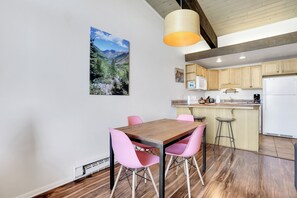 A dining area with a wooden table and pink chairs, a kitchen with wooden cabinets, and a hanging pendant light. - Lovely Ski in Ski out condo with amenities!!! (Steamboat Springs)