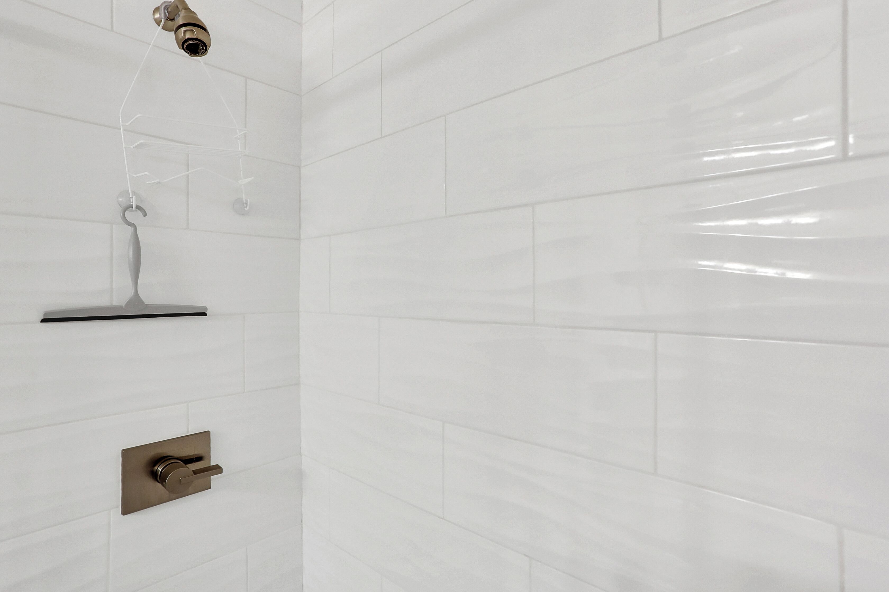 A bathroom with white tiled walls, a showerhead, and a faucet.