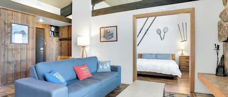 Un intérieur moderne avec un canapé bleu, un plancher en bois, un lit avec une couette blanche et une décoration murale sur le thème du ski.