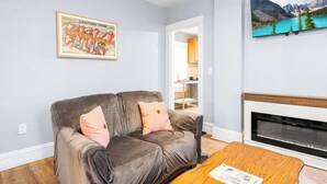 Una sala de estar con un sofá gris, una mesa de centro de madera, una chimenea y un cuadro enmarcado en la pared.