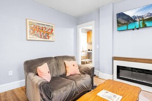 Ein Wohnzimmer mit grauem Sofa, einem Holztisch, einem Kamin und einem gerahmten Bild an der Wand.