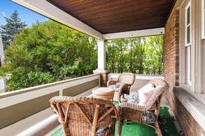 A covered balcony with wicker furniture and a view of greenery. - 2 Homes • Sleeps 12 • 6BR • 1 Mile to Falls (Niagara Falls)