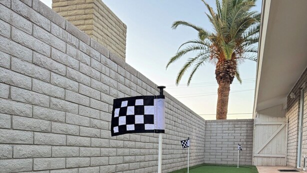 En minigolfbane med kunstgræs, ternede flag og en palme.