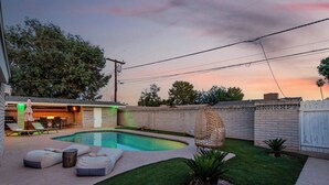 A backyard with a swimming pool, outdoor furniture, and a patio area.