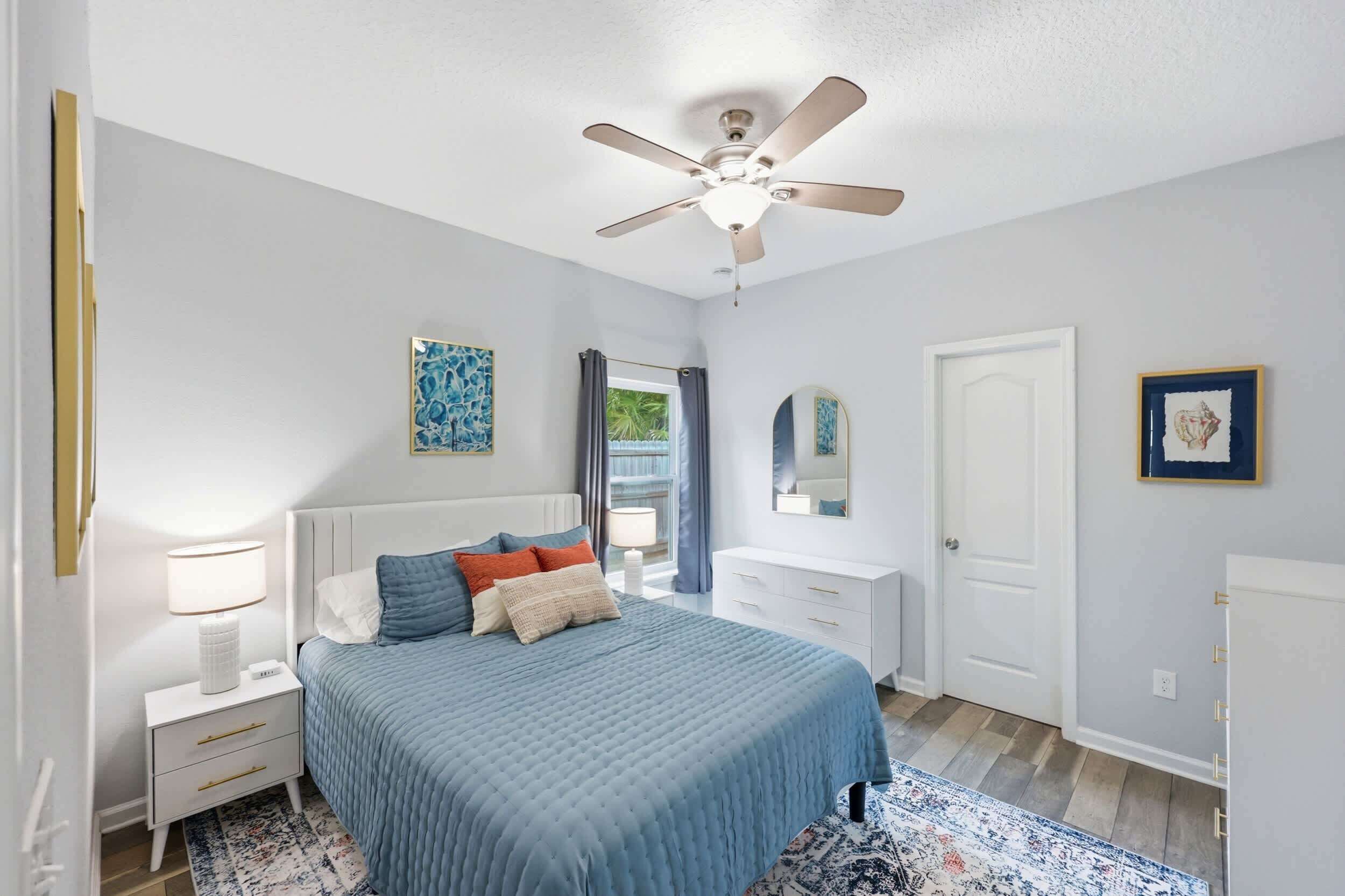 A bedroom with a bed, nightstands, a ceiling fan, a dresser, a mirror, and artwork on the walls.