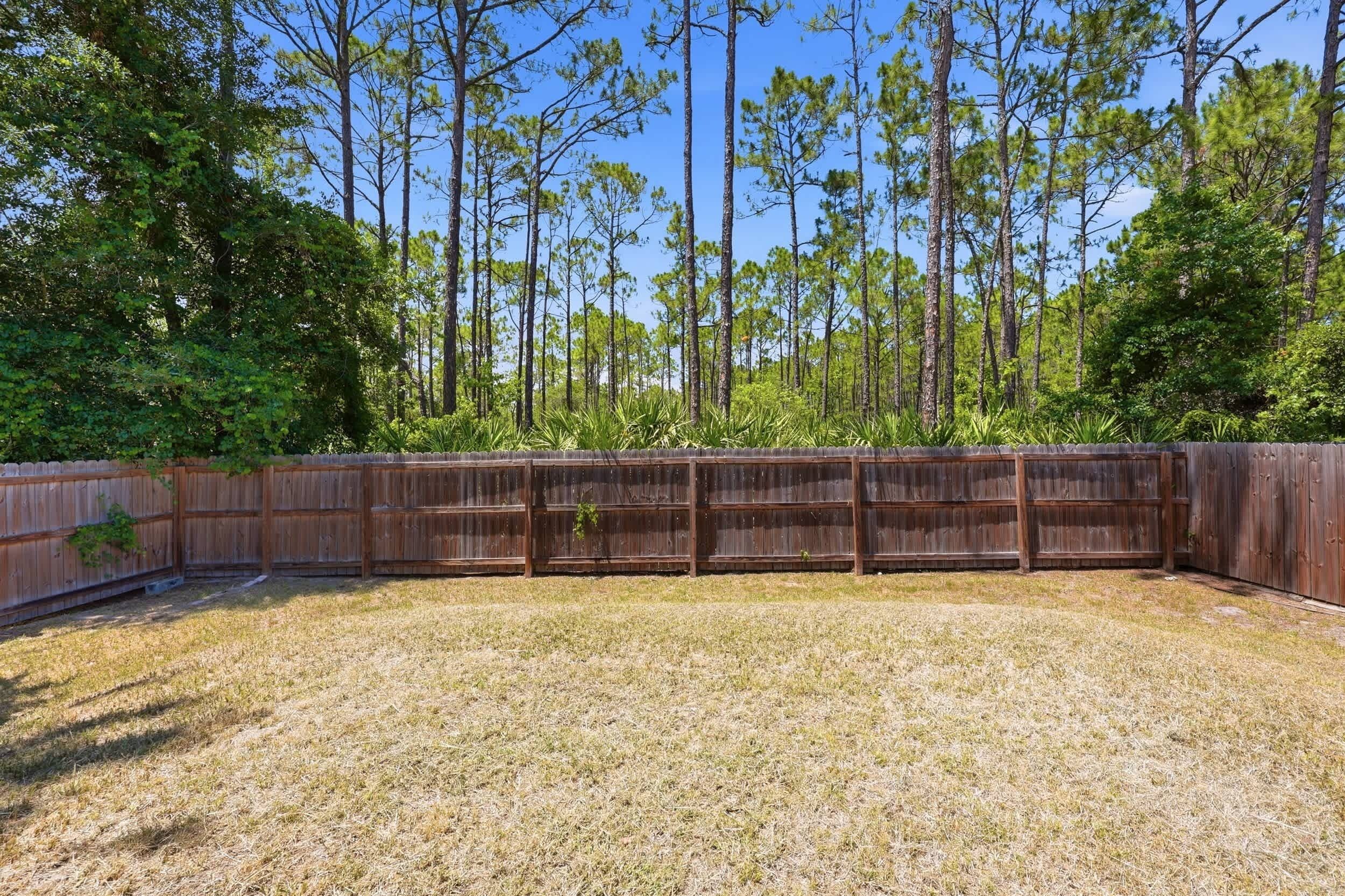 A fenced outdoor area with a grassy surface and tall trees in the background.