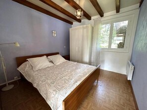 Ein Schlafzimmer mit einem hölzernen Bett, einem weißen Kleiderschrank, einer Stehlampe und einem Fenster mit Vorhängen.