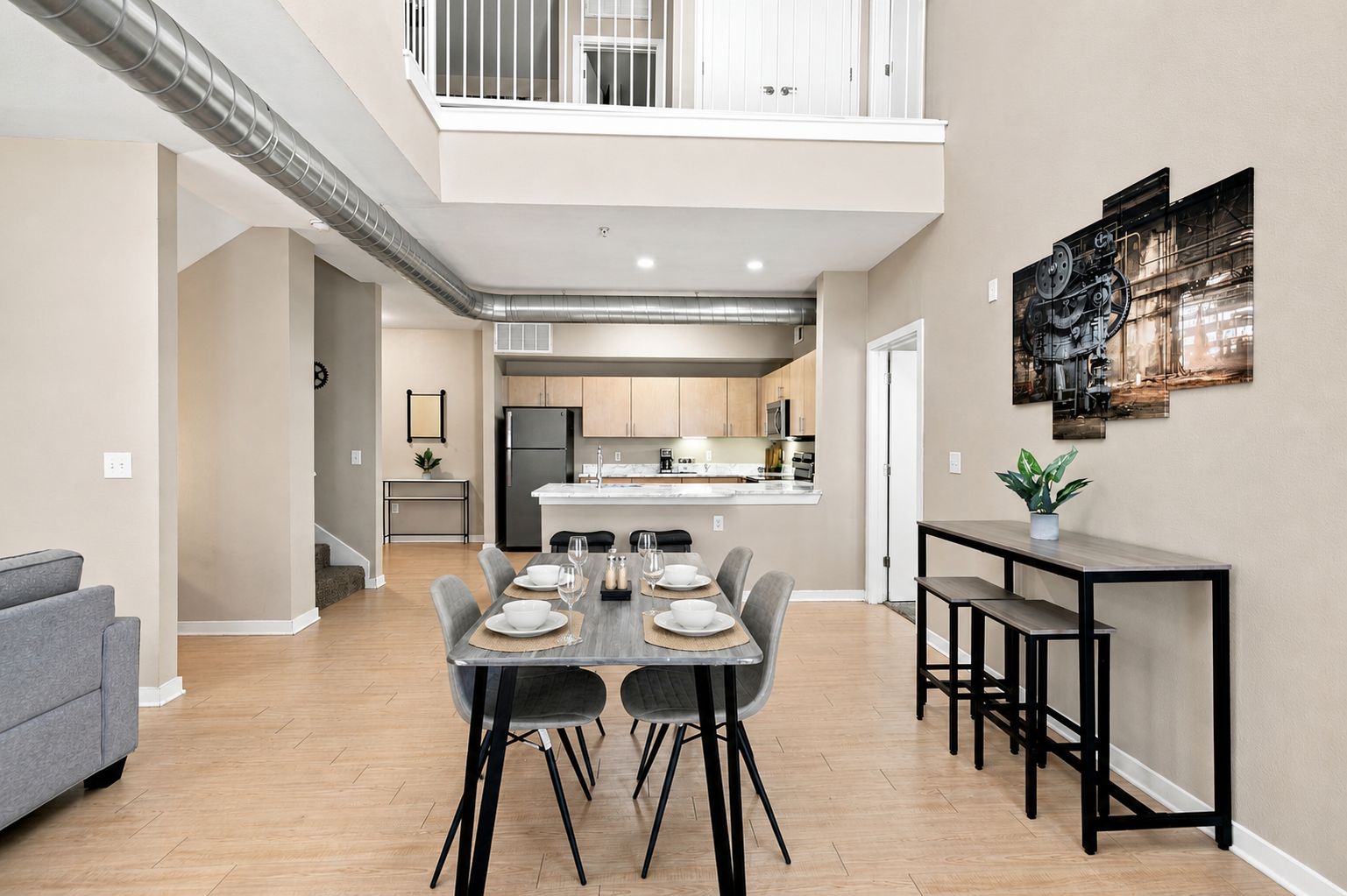 A modern kitchen with a central island, a dining area with a table set for four, and a balcony with white railings.