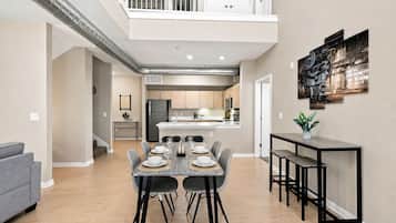 A modern kitchen with a central island, a dining area with a table set for four, and a balcony with white railings.