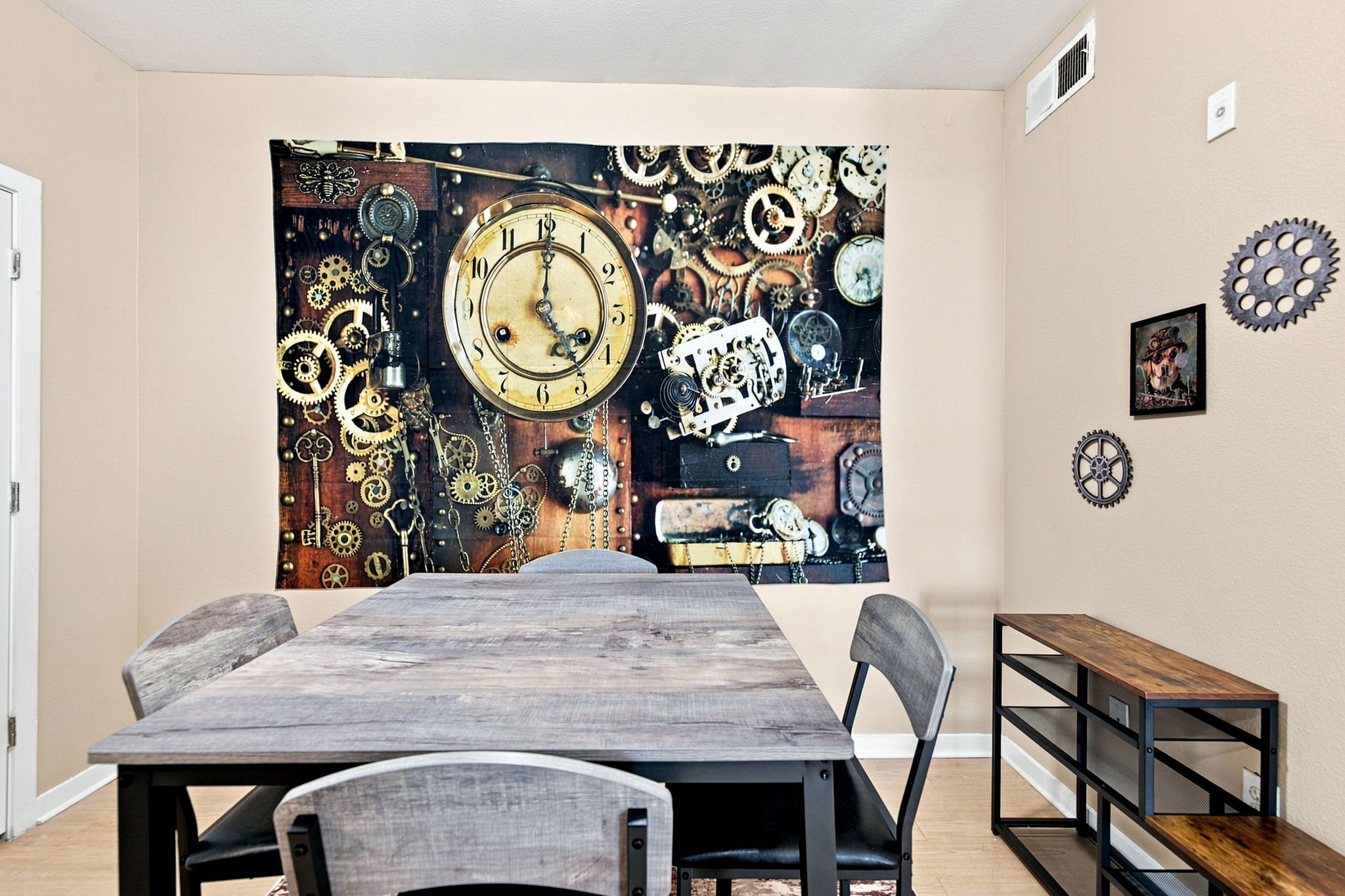 Un coin repas avec une table en bois, des chaises et une tapisserie murale représentant des engrenages et une horloge.