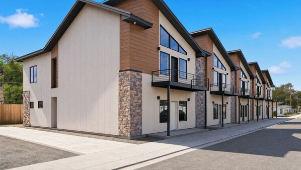 A modern multi-story residential building with balconies, a stone accent wall, and a clear sky.