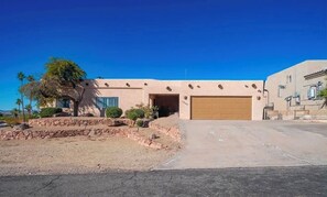 A building with a garage, a paved driveway, and a landscaped area with rocks and small trees. - Large home panoramic lake views, boat parking, pool, game room, ice machine! (Lake Havasu City)